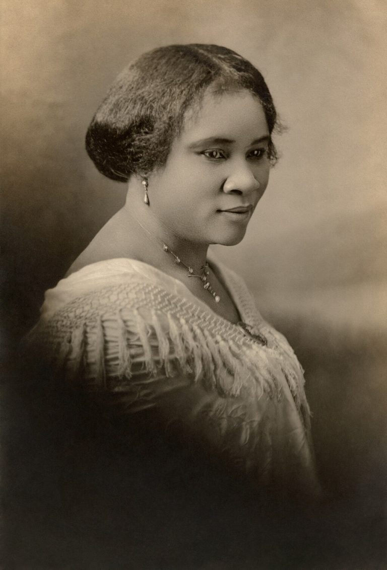 Black and white photographic bust length portrait of Madam C.J. Walker. Sitting sideways, her head is turned slightly right towards the viewer.